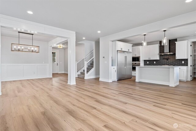 kitchen featuring white cabinetry, wall chimney exhaust hood, light wood-type flooring, a kitchen island, and built in appliances