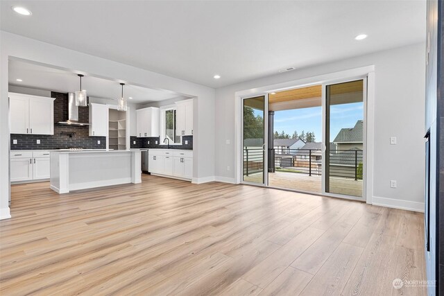 kitchen featuring wall chimney range hood, light wood-type flooring, and backsplash