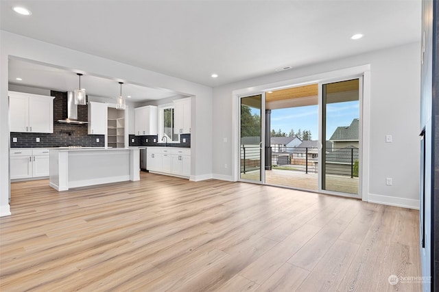 kitchen featuring tasteful backsplash, light wood-style flooring, stainless steel dishwasher, a sink, and wall chimney exhaust hood