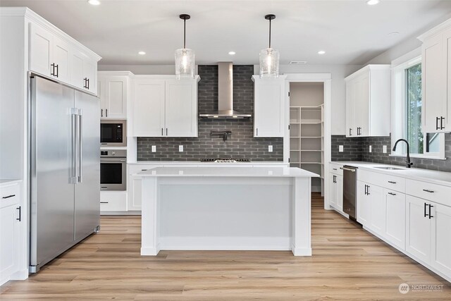 kitchen featuring light hardwood / wood-style flooring, decorative backsplash, wall chimney range hood, a kitchen island, and built in appliances