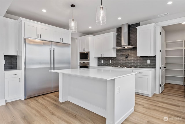 kitchen with light countertops, visible vents, wall chimney range hood, built in appliances, and light wood-type flooring