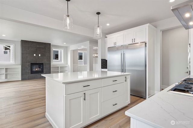 kitchen with decorative light fixtures, appliances with stainless steel finishes, light hardwood / wood-style flooring, a tiled fireplace, and white cabinetry