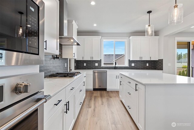 kitchen featuring backsplash, stainless steel appliances, white cabinetry, wall chimney exhaust hood, and light wood-type flooring