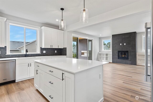 kitchen featuring white cabinets, stainless steel dishwasher, a tiled fireplace, and light hardwood / wood-style floors