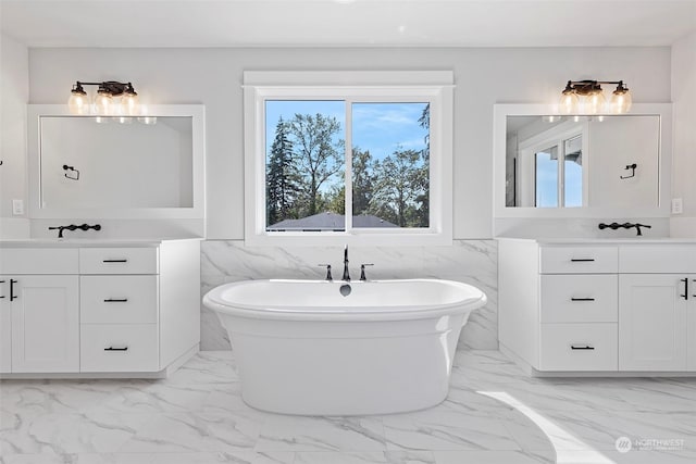 full bath with marble finish floor, two vanities, a freestanding bath, and tile walls