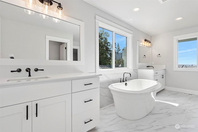 bathroom featuring recessed lighting, two vanities, a sink, a freestanding bath, and marble finish floor