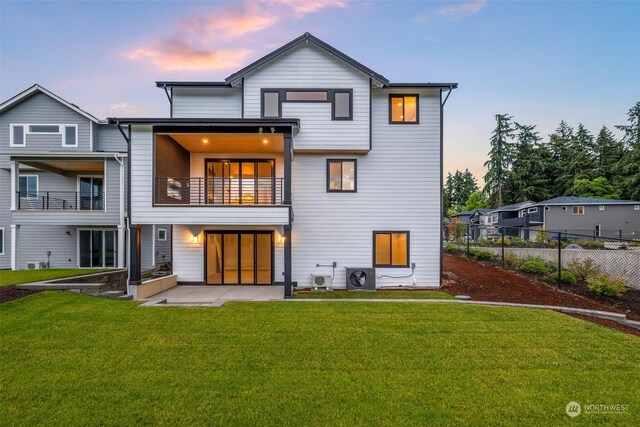 back house at dusk with a balcony, central air condition unit, a patio area, and a lawn