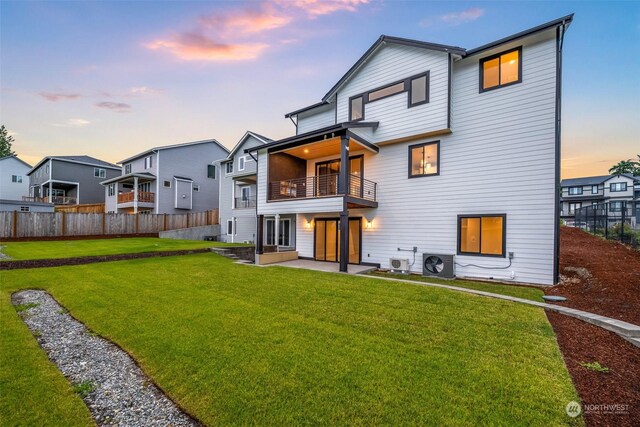 back house at dusk with a yard, central AC unit, and a balcony