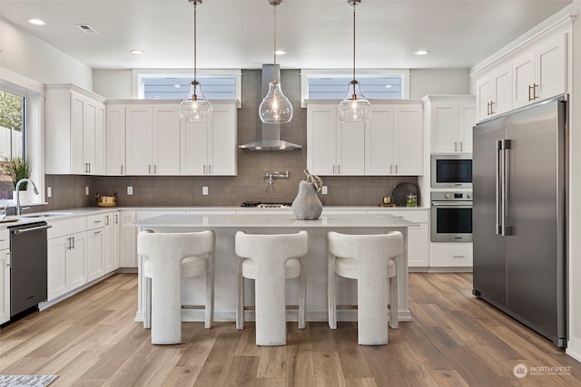 kitchen featuring light hardwood / wood-style flooring, built in appliances, wall chimney exhaust hood, and a center island