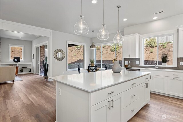 kitchen with a center island, light hardwood / wood-style floors, tasteful backsplash, white cabinetry, and pendant lighting