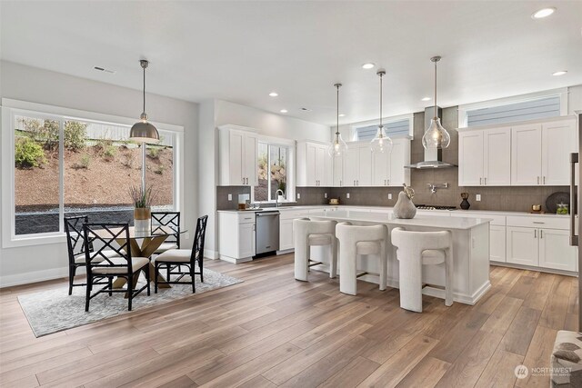 kitchen with plenty of natural light, wall chimney range hood, stainless steel dishwasher, and decorative light fixtures