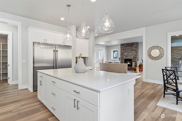 kitchen featuring light hardwood / wood-style flooring, pendant lighting, white cabinetry, a fireplace, and a center island