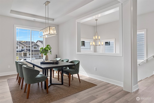 dining room with light wood-type flooring, a raised ceiling, and a chandelier