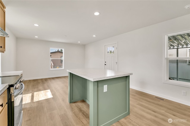 kitchen with light hardwood / wood-style floors, stainless steel range with electric cooktop, a kitchen island, and a healthy amount of sunlight