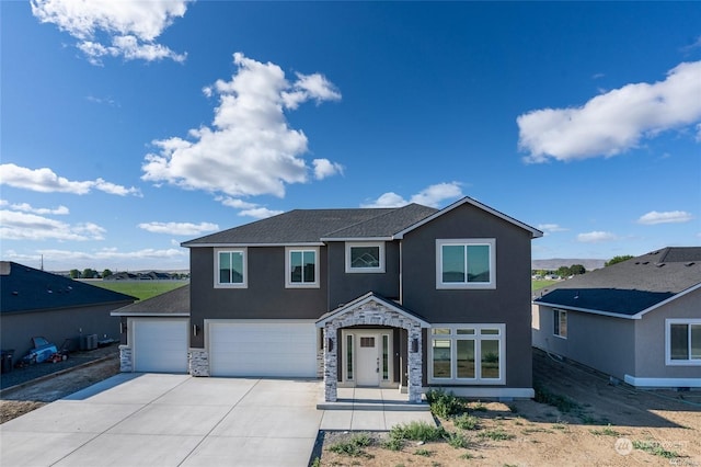 view of front of house with an attached garage, central AC, stone siding, driveway, and stucco siding