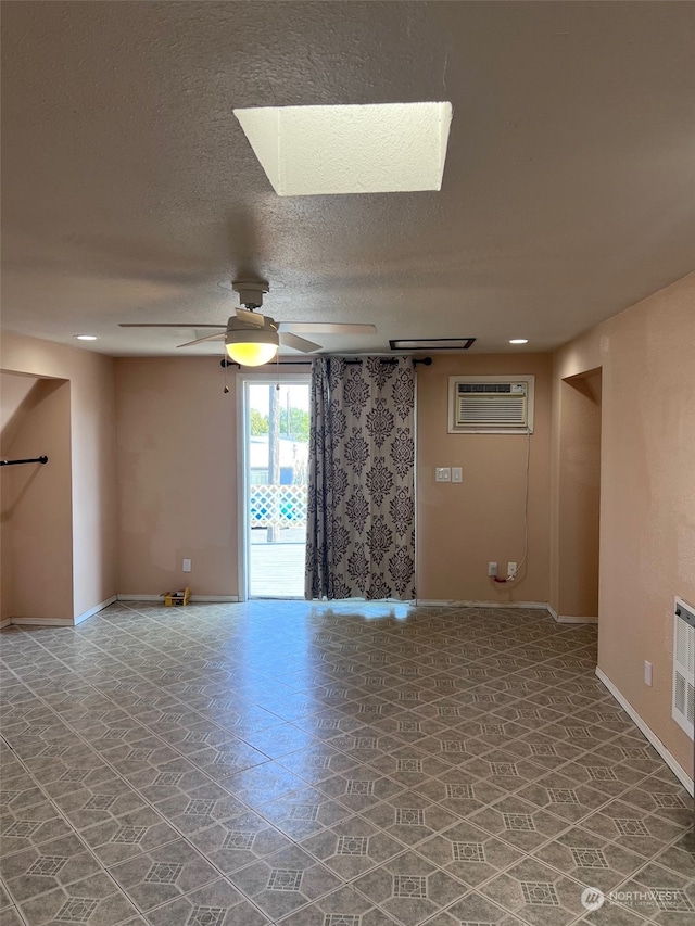 tiled spare room featuring ceiling fan, a wall mounted AC, a textured ceiling, and a skylight