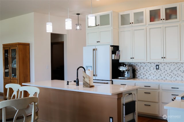 kitchen featuring hanging light fixtures, a kitchen breakfast bar, white cabinets, a center island with sink, and high end white fridge