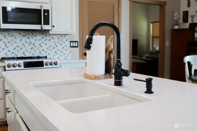 kitchen featuring white microwave, light countertops, decorative backsplash, white cabinets, and a sink