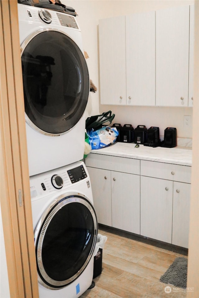 laundry room with cabinet space, light wood-style flooring, and stacked washing maching and dryer