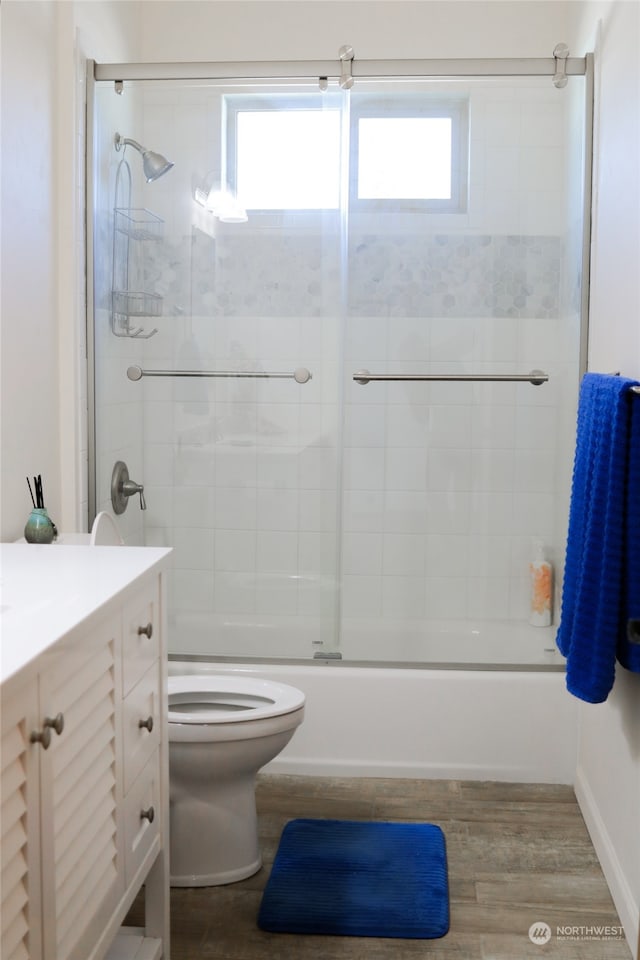 full bathroom with vanity, hardwood / wood-style floors, shower / bath combination with glass door, and toilet