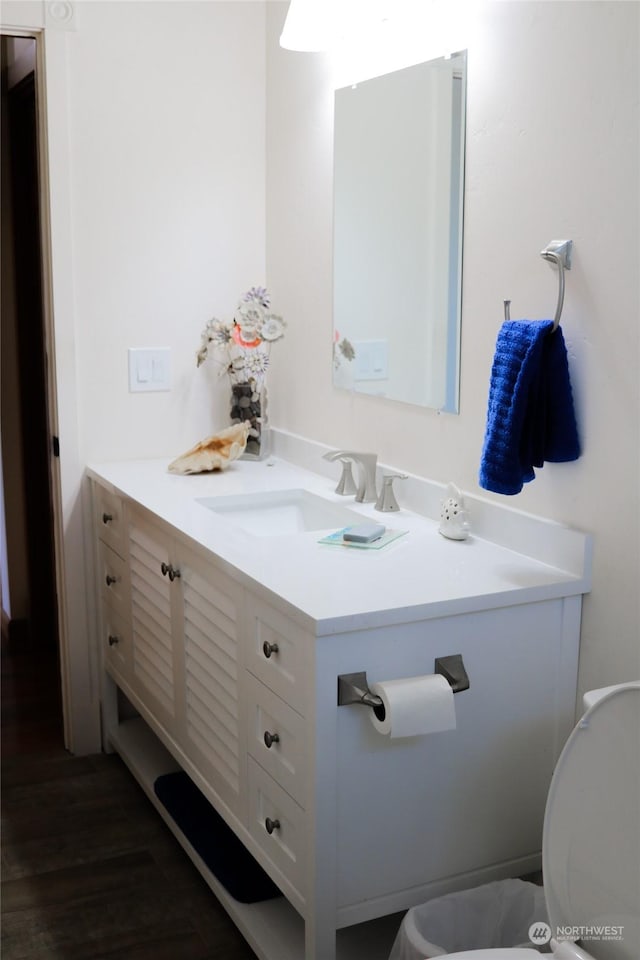 half bathroom with toilet, vanity, and wood finished floors