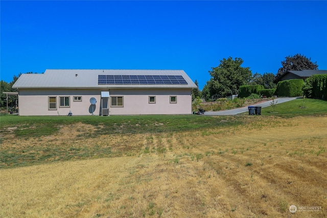 back of property with stucco siding, a yard, and solar panels