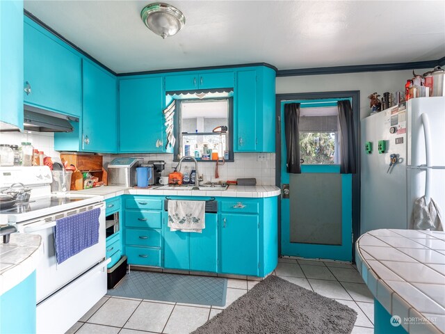 kitchen with light tile patterned floors, backsplash, blue cabinetry, and white appliances