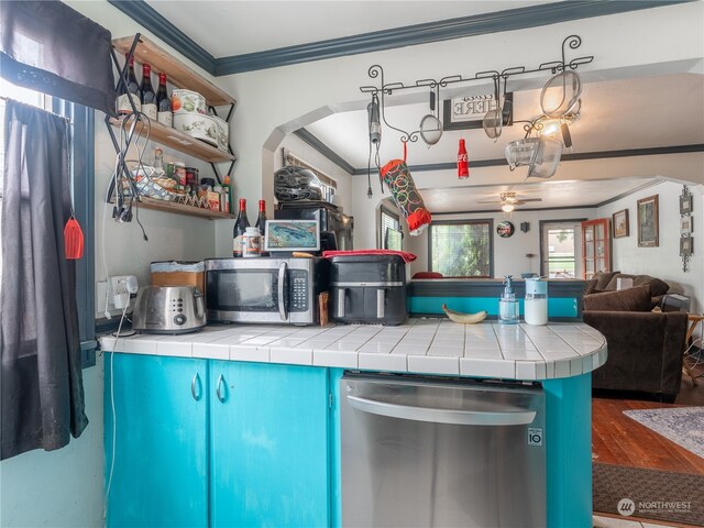 kitchen featuring stainless steel appliances, ornamental molding, tile counters, wood-type flooring, and ceiling fan