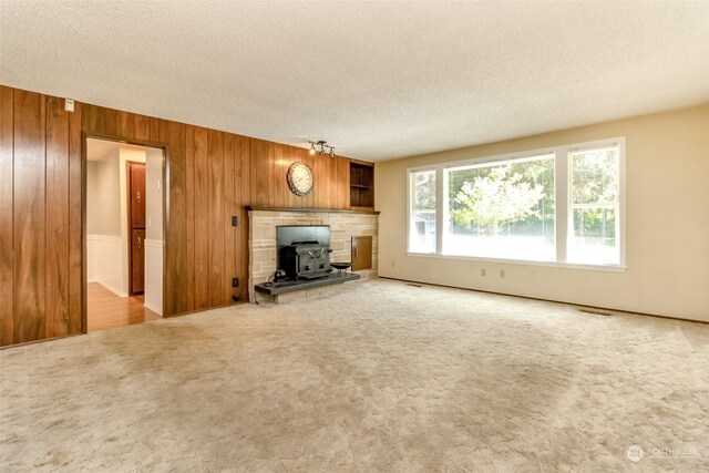 unfurnished living room with a textured ceiling, wood walls, a wood stove, and carpet flooring