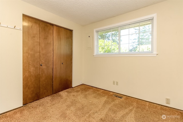 unfurnished bedroom with a textured ceiling, light colored carpet, and a closet