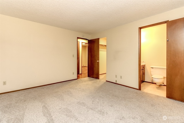 unfurnished bedroom with a textured ceiling, ensuite bath, and light carpet