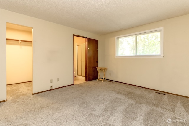 unfurnished bedroom featuring a textured ceiling, a closet, light carpet, and a spacious closet