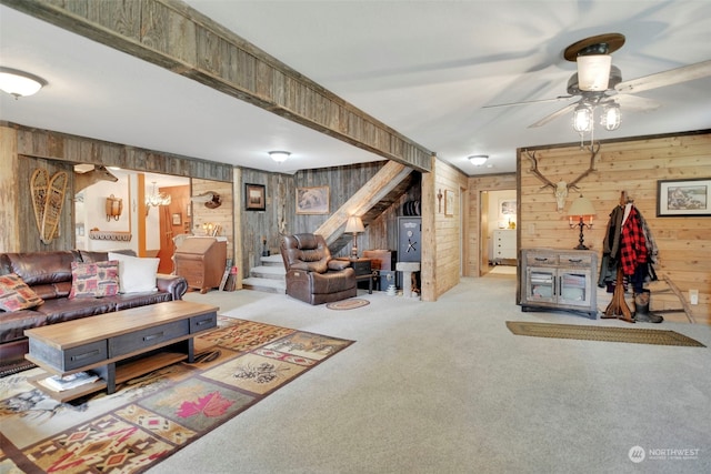 living area with light carpet, ceiling fan, wooden walls, and stairs