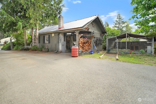 exterior space with metal roof, aphalt driveway, a chimney, and an outdoor structure