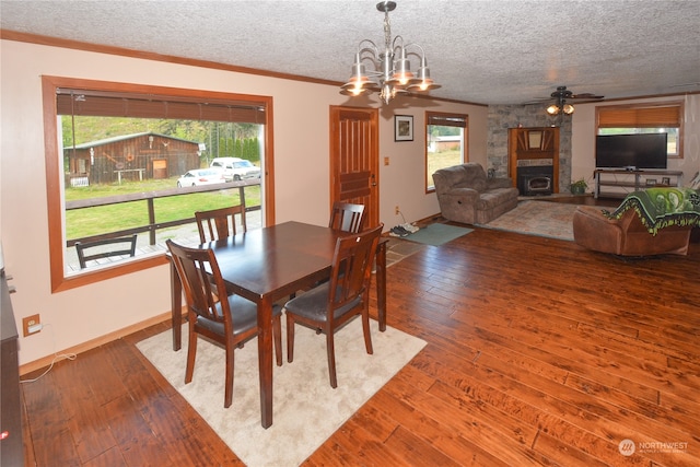 dining area featuring hardwood / wood-style floors, ceiling fan with notable chandelier, a textured ceiling, and a stone fireplace