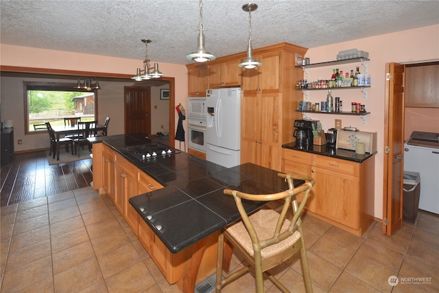 kitchen with white appliances, tile counters, a breakfast bar, washer / dryer, and light wood-type flooring