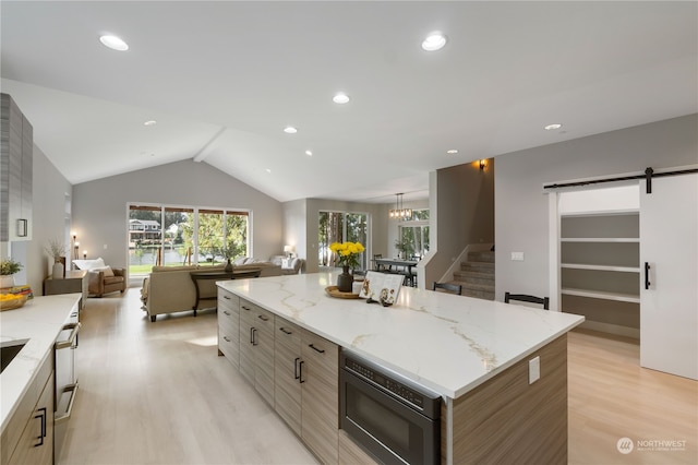 kitchen featuring a kitchen island, black microwave, a barn door, light wood-type flooring, and vaulted ceiling