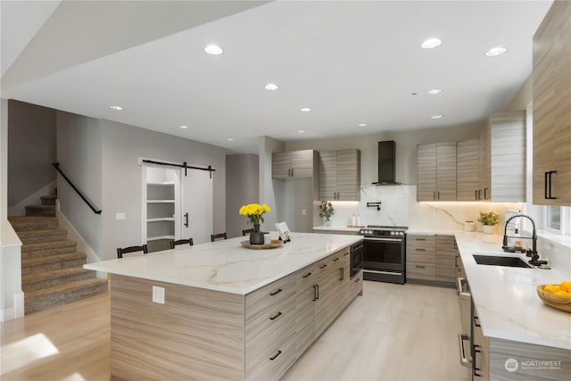 kitchen featuring light stone countertops, a center island, stainless steel range oven, wall chimney range hood, and a barn door