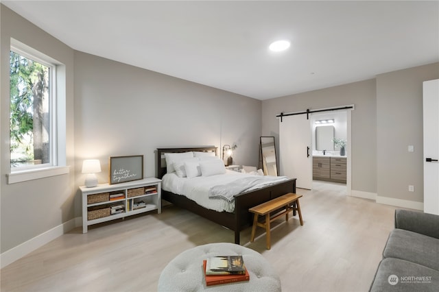 bedroom featuring ensuite bathroom, a barn door, and light hardwood / wood-style floors