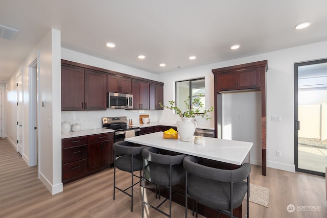 kitchen featuring appliances with stainless steel finishes, a kitchen breakfast bar, tasteful backsplash, light hardwood / wood-style flooring, and a kitchen island