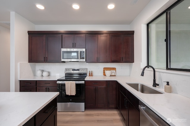 kitchen with dark brown cabinetry, sink, stainless steel appliances, light stone counters, and light wood-type flooring