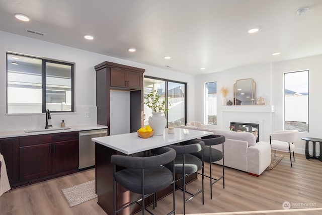 kitchen with dark brown cabinetry, sink, dishwasher, light hardwood / wood-style floors, and a breakfast bar area