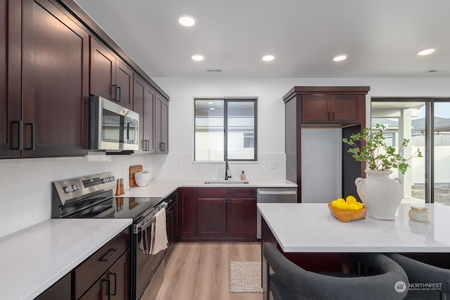 kitchen featuring light stone countertops, appliances with stainless steel finishes, a kitchen bar, sink, and light hardwood / wood-style flooring