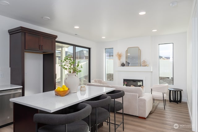 kitchen with a kitchen breakfast bar, light wood-type flooring, dark brown cabinetry, dishwasher, and a kitchen island