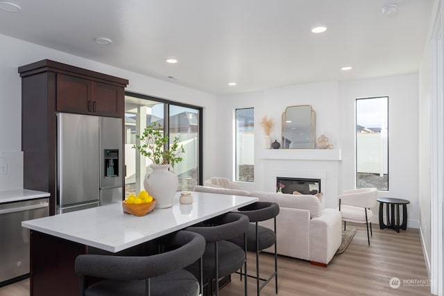 kitchen with appliances with stainless steel finishes, a kitchen breakfast bar, dark brown cabinets, light hardwood / wood-style floors, and a kitchen island