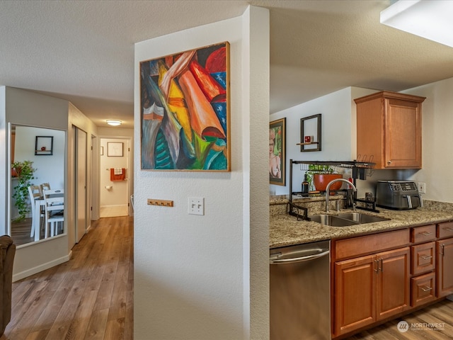 kitchen with light wood-type flooring, a textured ceiling, stainless steel dishwasher, and sink