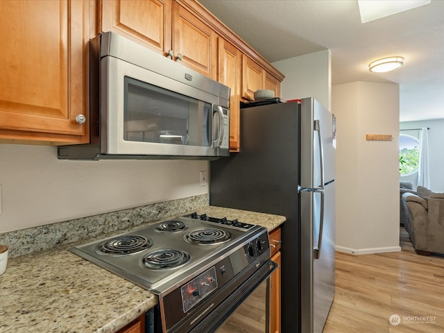 kitchen with stove, light wood-type flooring, and light stone countertops