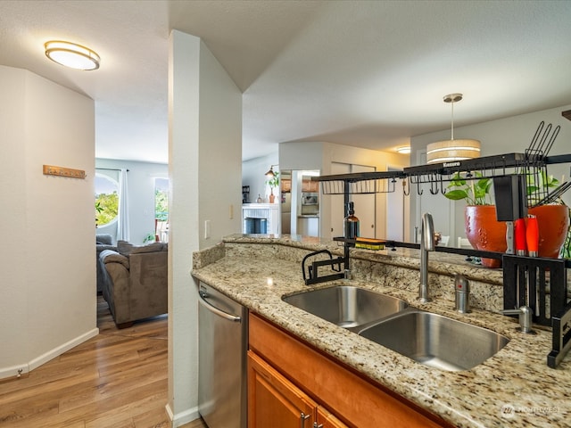 kitchen featuring light wood-type flooring, decorative light fixtures, light stone countertops, sink, and stainless steel dishwasher