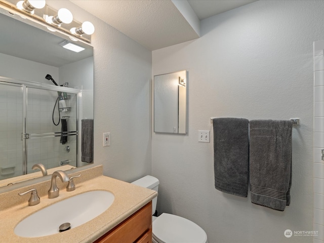 bathroom featuring vanity, toilet, a shower with shower door, and a textured ceiling