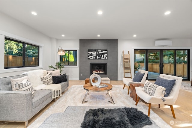 living room with a wall mounted AC, light hardwood / wood-style flooring, and a tile fireplace